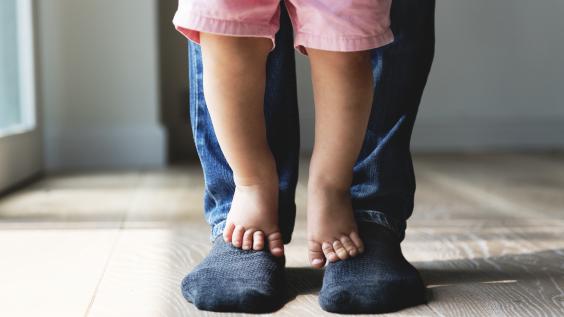 A child stands on parent's feet.