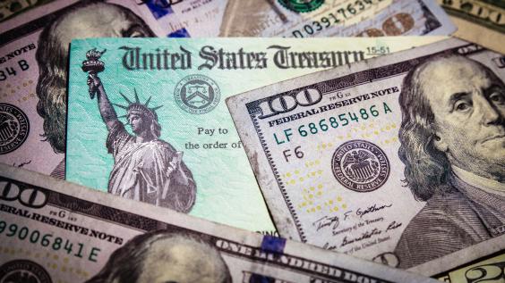 A stimulus check lies amongst hundred dollar bills.