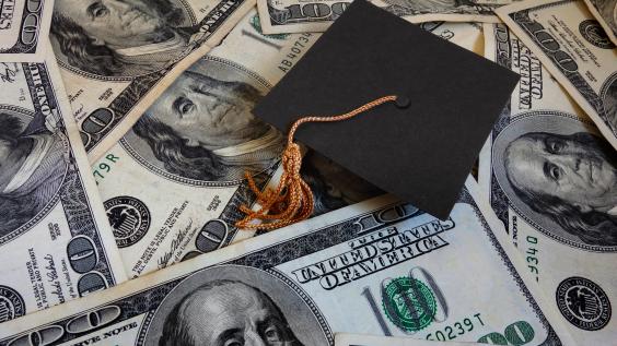 A graduation cap lies amongst $100 bills.