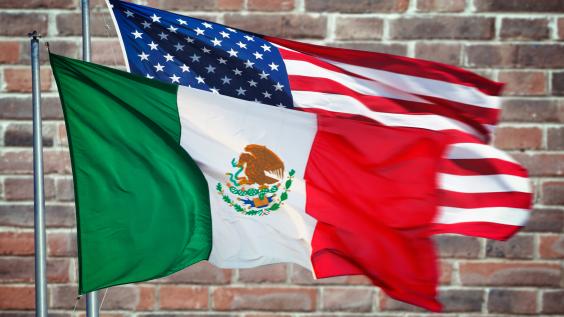 The Mexico and U.S. flags in front of a brick wall.