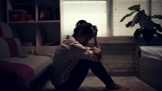 A woman sits on the floor while looking down.