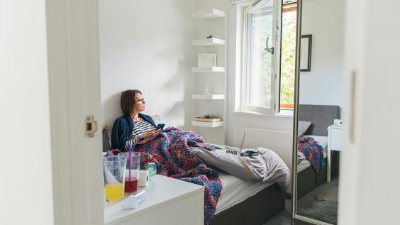 A woman lies in bed while looking out a window.