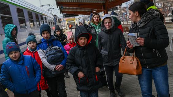 Ukrainian refugees walk down a street with their belongings.