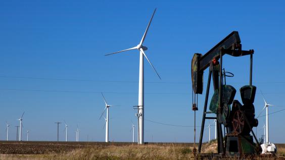 An oil pump works next to wind turbines in a field.