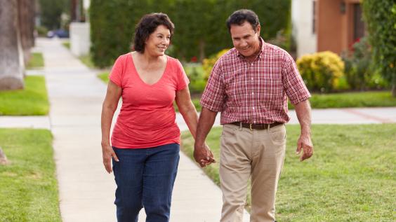 A Hispanic senior couple walks through a neighborhood.