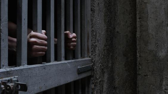 A prisoner grabs onto the bars of a jail cell.