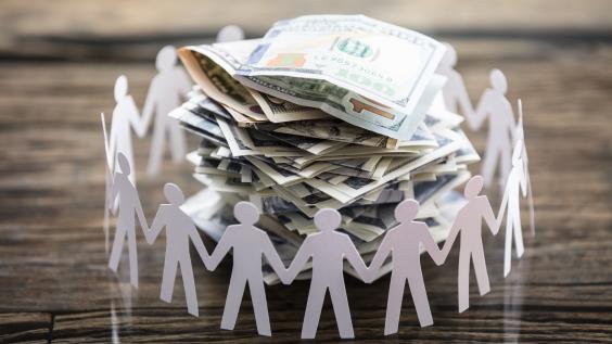 Paper cut-outs of people surrounding a pile of cash.