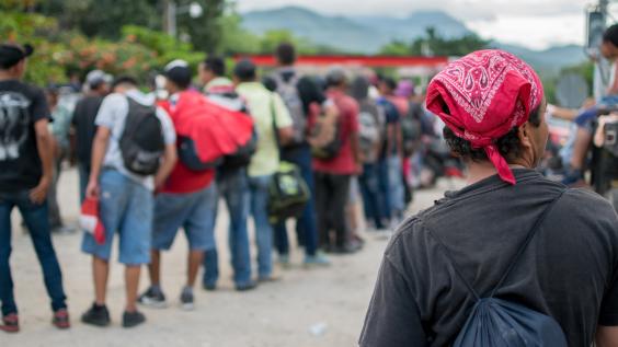 Line of Hispanic immigrants waiting outside with backs to viewer.