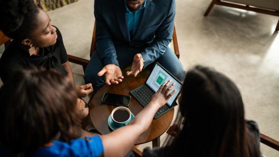 Four people discussing business around a table with coffee.