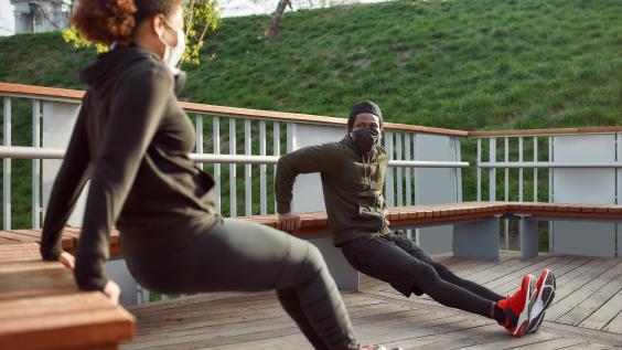 Two individuals in masks doing tricep exercises outdoors.