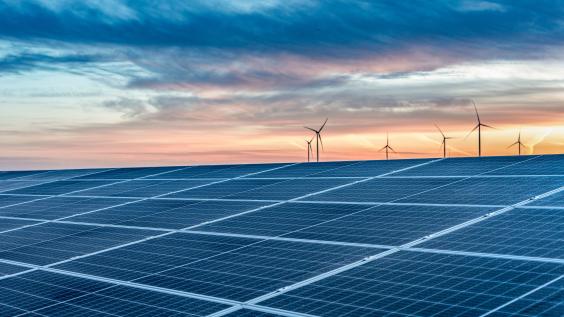 Solar panels with wind turbines in the distance at sundown.
