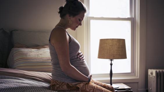Pregnant woman sitting on bed, cradling belly 