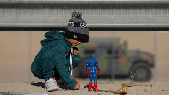Child at border plays in the dirt with superhero toy