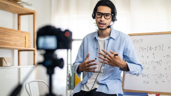 A teacher records a video for a remote class in front of a camera.