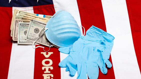 A mask, gloves, money, and letters spelling "vote" lie on a flag of the United States.