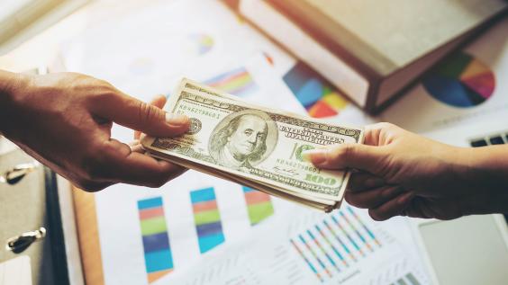 Close up of hands and business giving as illustrated by the exchange of US currency