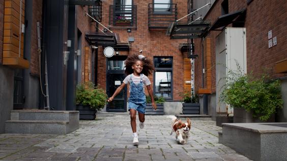 Child running alongside dog in city environment