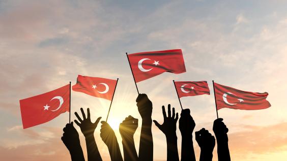 Turkish flags held up by hands against the sky