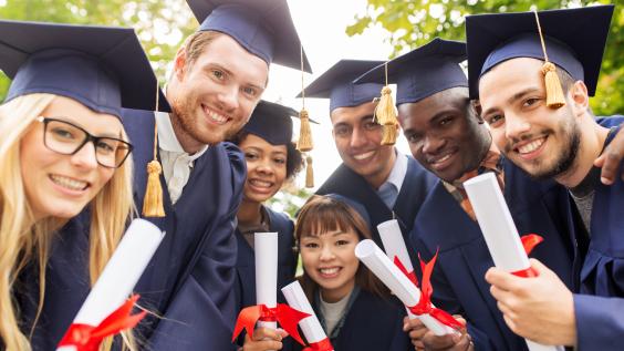 Smiling young graduates in gowns and mortarboards clutching diplomas