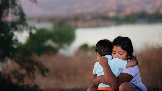 Brother and sister separated from parents are hugging each other in a foreign country, across a river. 