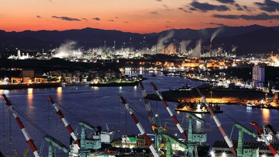 Night view of shipyard with tower cranes near the sea against chimney of oil refinery factory.