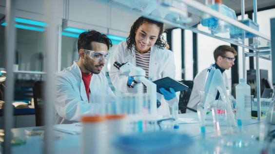 Modern Medical Research Laboratory, Young Scientists Using Microscope, Digital Tablet, Doing Sample Analysis, Talking. Diverse Team of Specialists work in Advanced Lab.