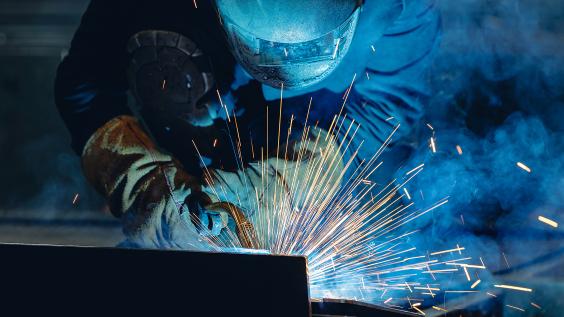 Industrial welder at work with sparks flying in shipyard setting.