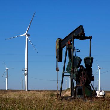 An oil pump works next to wind turbines in a field.