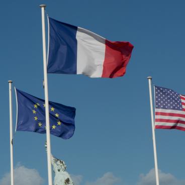 The flags of the EU, France, and the United States wave together in the air.