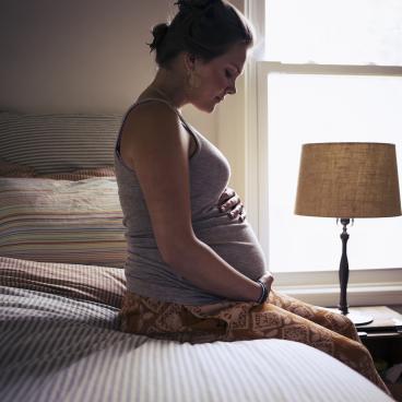 Pregnant woman sitting on bed, cradling belly 
