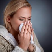 A woman sneezes into a tissue.