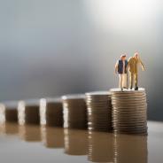 Two old people standing on a stack of coins.