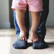 A child stands on parent's feet.