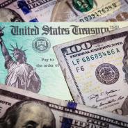 A stimulus check lies amongst hundred dollar bills.