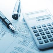 A calculator and fountain pen lie on top of accounting documents.