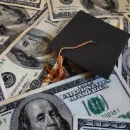 A graduation cap lies amongst $100 bills.