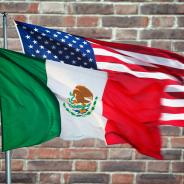 The Mexico and U.S. flags in front of a brick wall.