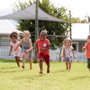 Five children run across a lawn.