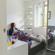 A woman lies in bed while looking out a window.