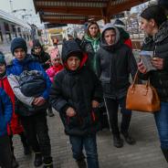 Ukrainian refugees walk down a street with their belongings.