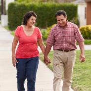 A Hispanic senior couple walks through a neighborhood.