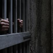 A prisoner grabs onto the bars of a jail cell.