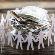 Paper cut-outs of people surrounding a pile of cash.