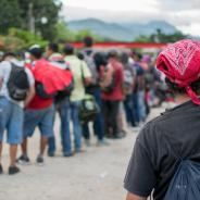 Line of Hispanic immigrants waiting outside with backs to viewer.