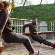 Two individuals in masks doing tricep exercises outdoors.