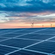 Solar panels with wind turbines in the distance at sundown.