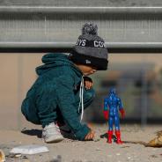 Child at border plays in the dirt with superhero toy