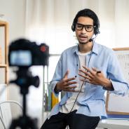 A teacher records a video for a remote class in front of a camera.