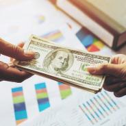 Close up of hands and business giving as illustrated by the exchange of US currency