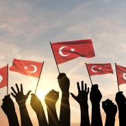 Turkish flags held up by hands against the sky